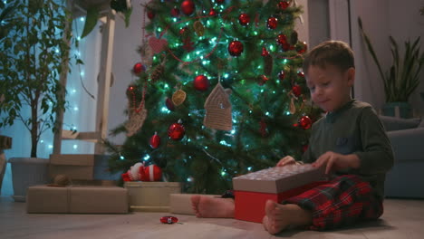 Ein-Glücklich-Lächelnder-Kleiner-Junge-öffnet-Sein-Weihnachtsgeschenk-Vom-Weihnachtsmann.-Junge-öffnet-Weihnachtsgeschenk-Zu-Hause.-Hochwertiges-4K-Filmmaterial